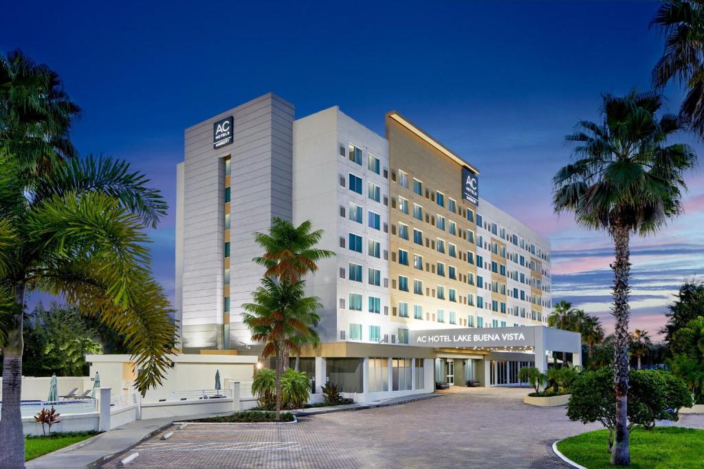 a large white building with palm trees in front of it at AC Hotel by Marriott Orlando Lake Buena Vista in Orlando