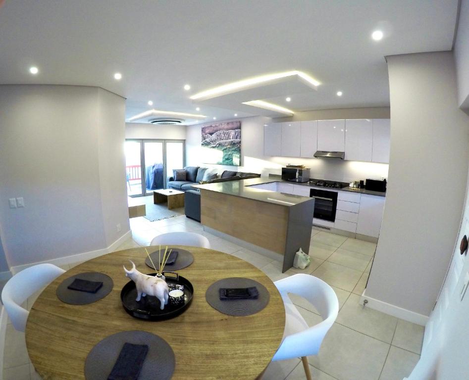 a kitchen and dining room with a wooden table and chairs at Stylish Sea View Apartment in Santorini Estate. in Ballito