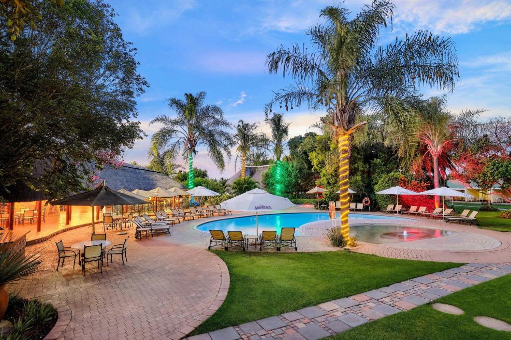 basen ze stołami i krzesłami oraz palmą w obiekcie Protea Hotel by Marriott Polokwane Ranch Resort w mieście Polokwane