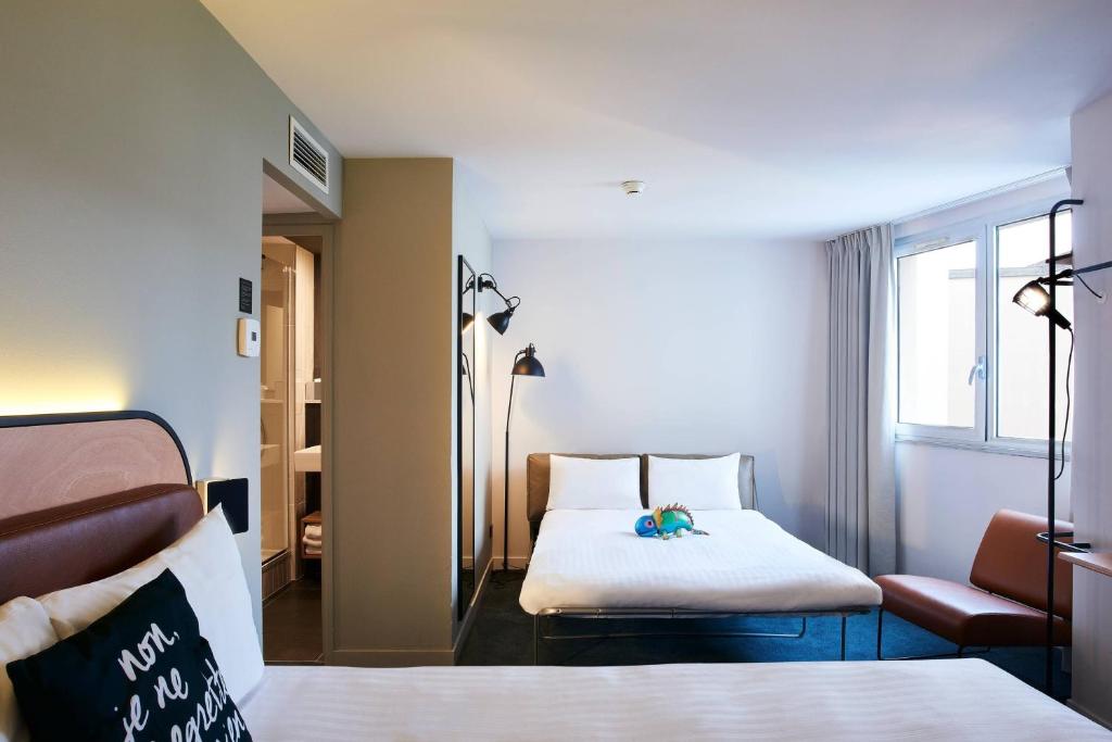 a hotel room with two beds and a chair at Moxy Paris Bastille in Paris