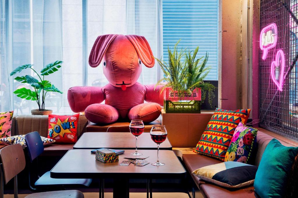 a room with a pink chair and two glasses of wine at Moxy Paris Bastille in Paris