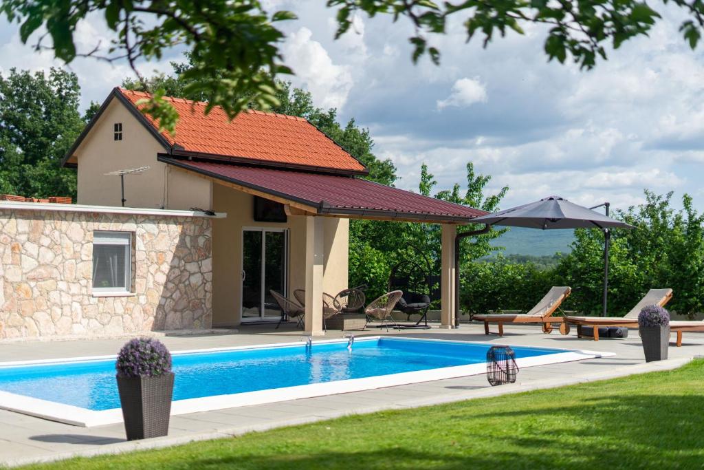 a swimming pool with a house and an umbrella at Kuca za odmor Sliskovic 
