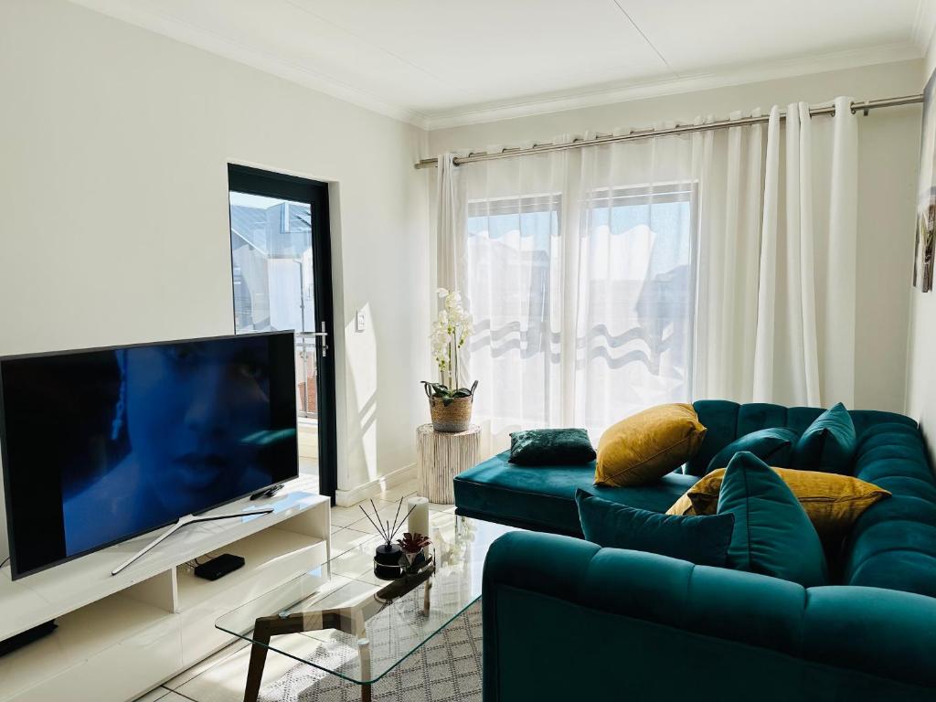 ein Wohnzimmer mit einem blauen Sofa und einem Flachbild-TV in der Unterkunft The Blyde, an impeccable blissful getaway (Balwin properties) in Pretoria