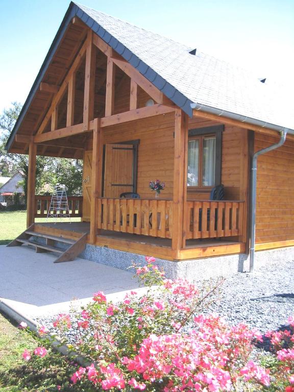 eine große Holzhütte mit einer Veranda und Blumen in der Unterkunft Chalets du Lac in Arcizans-Avant