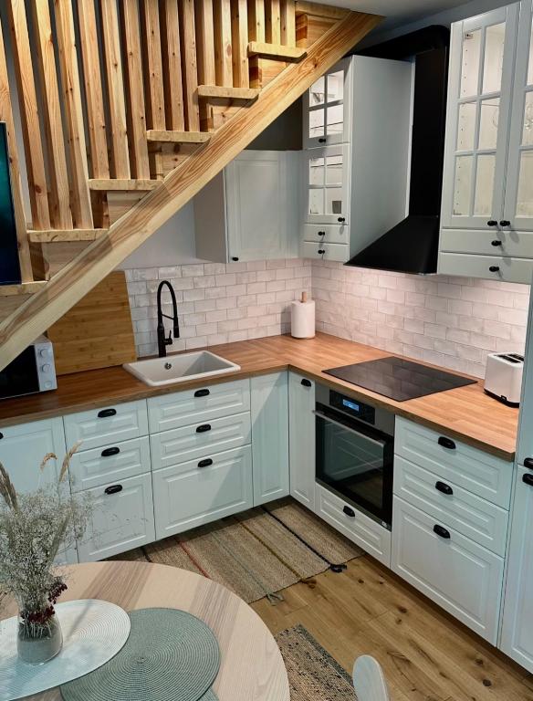 a kitchen with white cabinets and a wooden staircase at Rugio namai-Rye house in Palanga