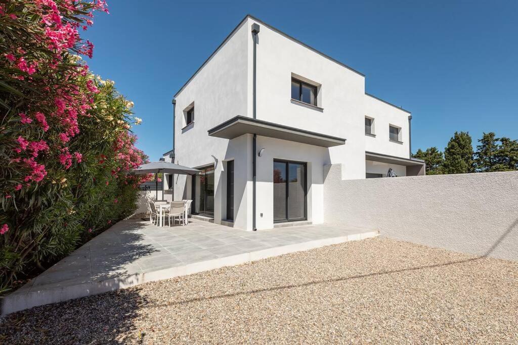une maison blanche avec des tables et des chaises devant elle dans l'établissement Villa MOON - 600m plage - clim - 6 pers - Cap d'Agde, au Cap d'Agde