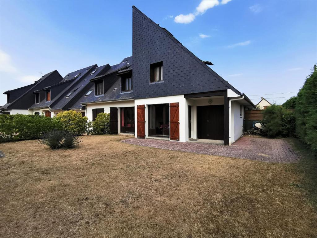 une maison avec un toit noir et une cour dans l'établissement Cottage à 2 mn à pied de la mer, à Merville-Franceville-Plage