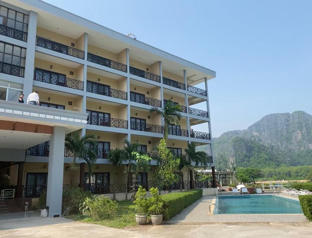 a hotel with a swimming pool and mountains in the background at Lisha The Grand Riverside Hotel in Vang Vieng