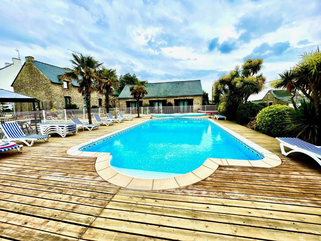 a swimming pool on a wooden deck with chairs and a house at Gîtes et Chambres - Les Buissonnets in La Turballe