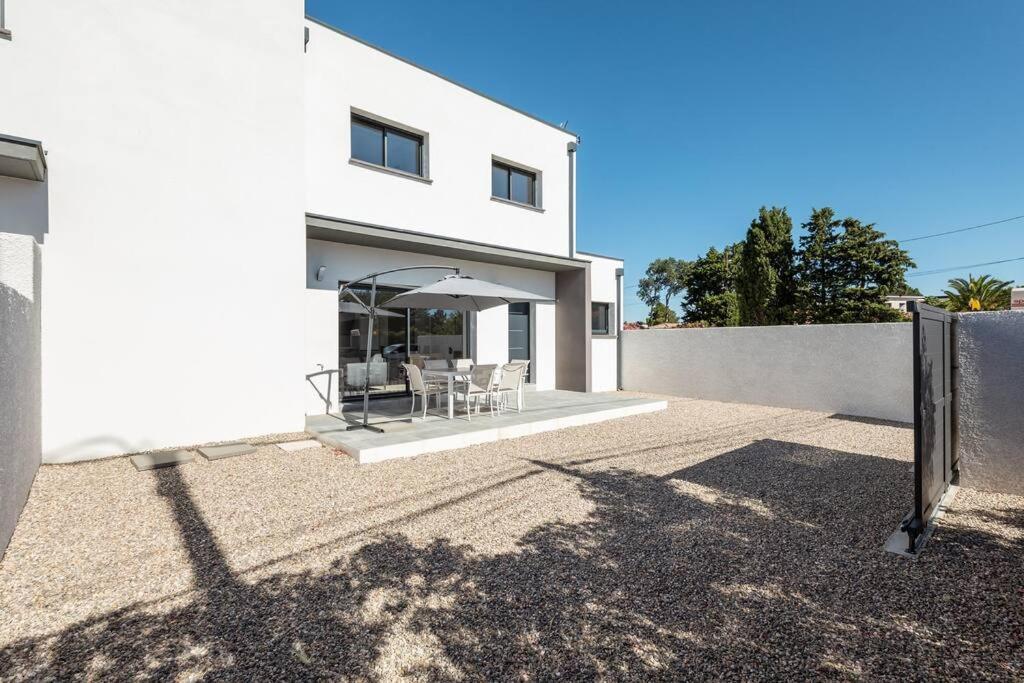 Cette maison blanche dispose d'une terrasse avec un parasol. dans l'établissement Villa SUN - 600m plage - clim - 6 pers - Cap d'Agde, au Cap d'Agde