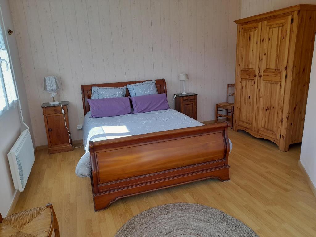 1 dormitorio con cama de madera y almohadas moradas en Chambre d'hôtes de l'Ancienne école, en RiviÃ¨res