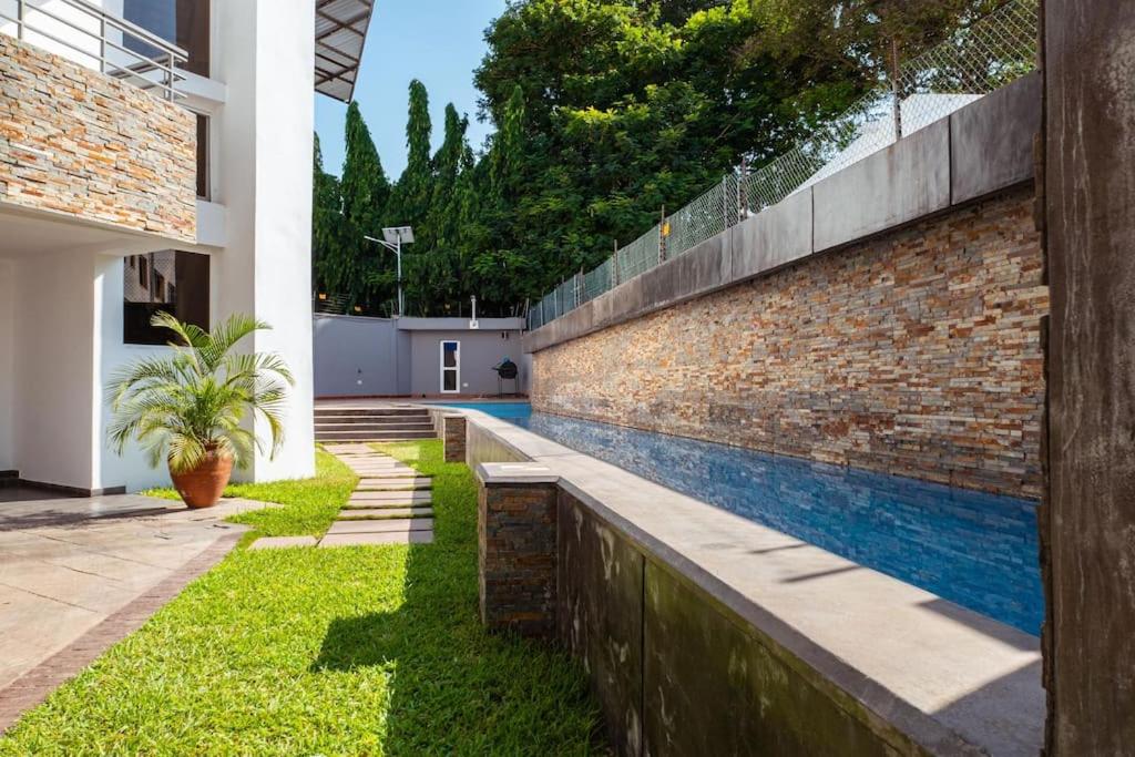 a brick wall with a swimming pool next to a house at Luxurious and peaceful 3BR Apt with a Pool Close to shops, restaurants, Kotoka Airport in Accra
