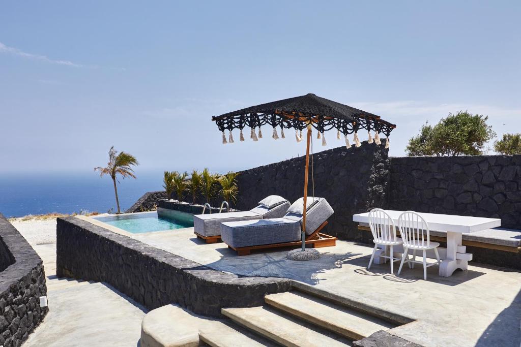 eine Terrasse mit einem Tisch, Stühlen und einem Sonnenschirm in der Unterkunft Theano Cave Suites & Villas in Imerovigli
