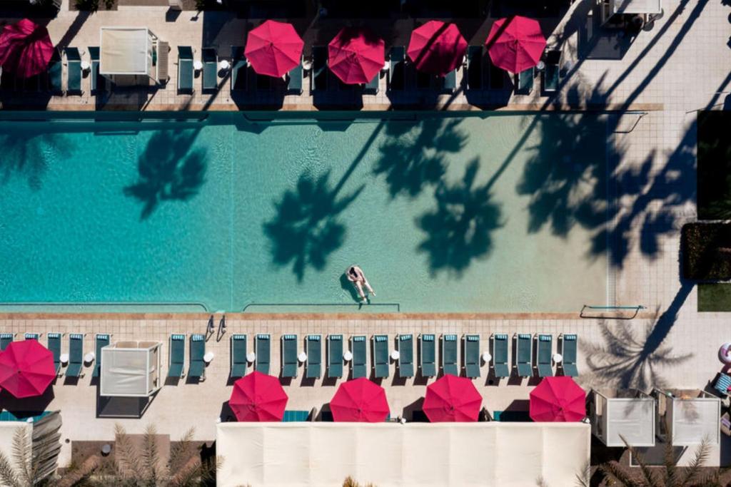 a swimming pool with red umbrellas and a person sitting on a chaise at Hotel Adeline, Scottsdale, a Tribute Portfolio Hotel in Scottsdale
