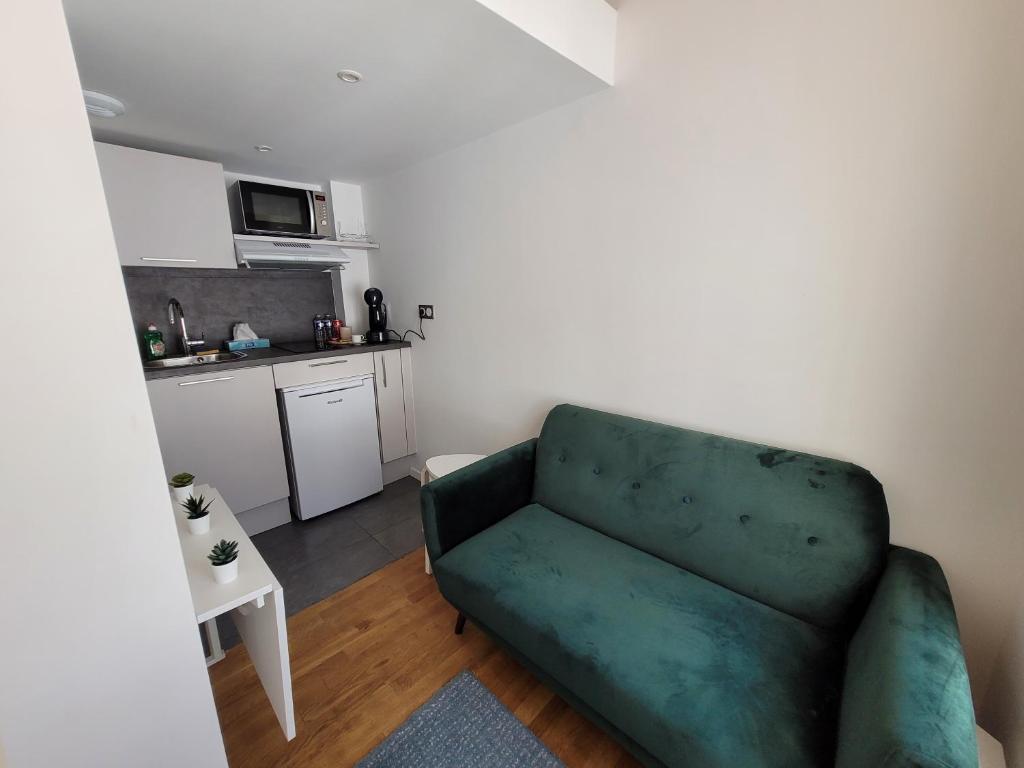 a living room with a green couch and a kitchen at 2G- Studio tout équipé avec cuisine proche Paris in Issy-les-Moulineaux