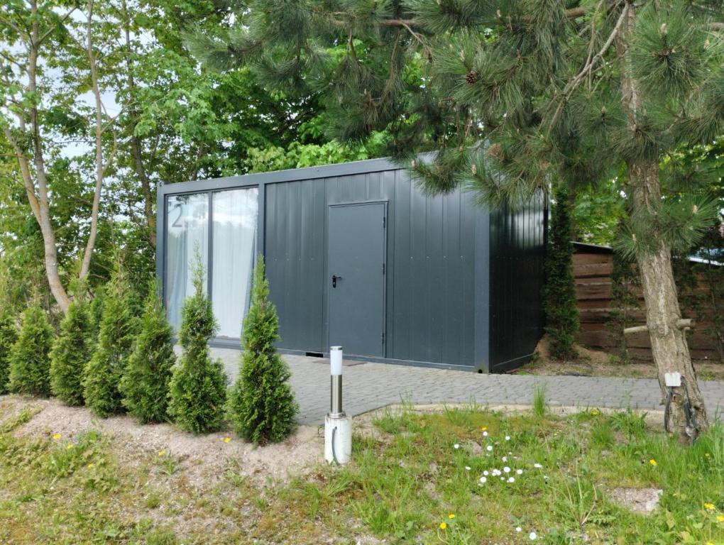 ein graues Gebäude mit einer Tür und einigen Bäumen in der Unterkunft Šaltupio kaimo turizmas 