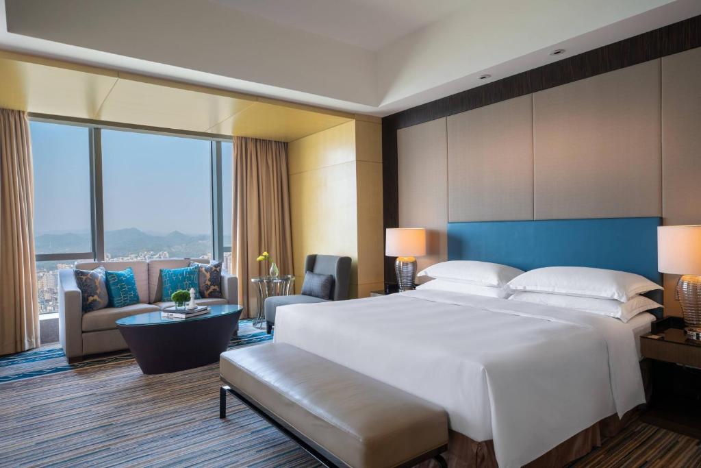 a bedroom with a large white bed and a living room at Renaissance Huizhou Hotel in Huizhou