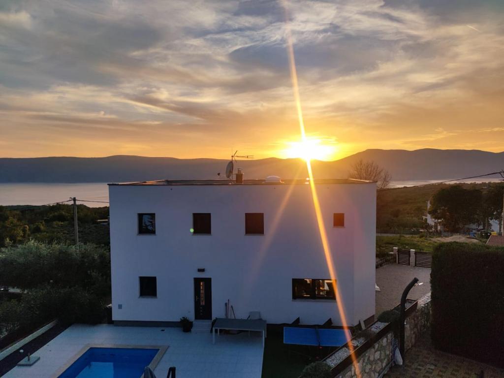 a sunset over a white house with a swimming pool at Villa Alma Krk in Linardići