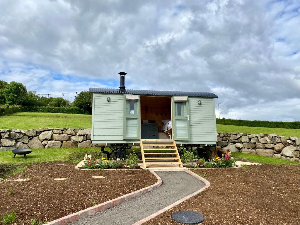 a green tiny house in a field with a stone wall at The Stone Wall Hideaway in Portglenone