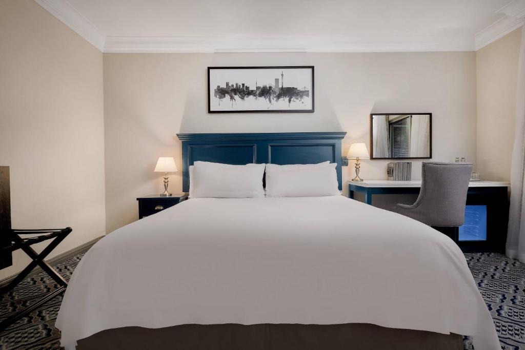 a bedroom with a large white bed and two chairs at Protea Hotel by Marriott Johannesburg Balalaika Sandton in Johannesburg
