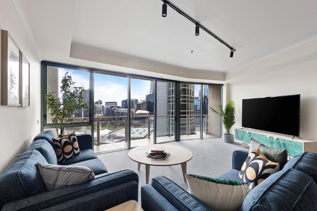 Nook Melbourne Apartments في ملبورن: غرفة معيشة مع اثنين من الأرائك الزرقاء وتلفزيون