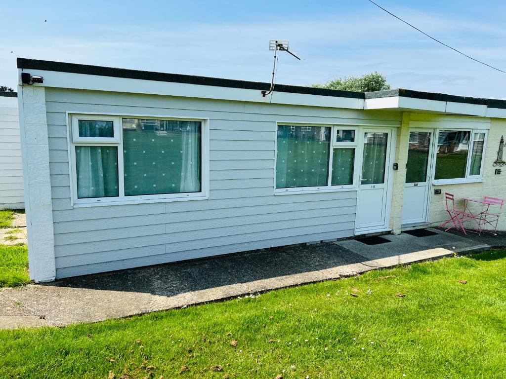 a small white house with a table and a chair at 2 Bedroom Chalet SB113, Sandown Bay, Isle of Wight in Brading