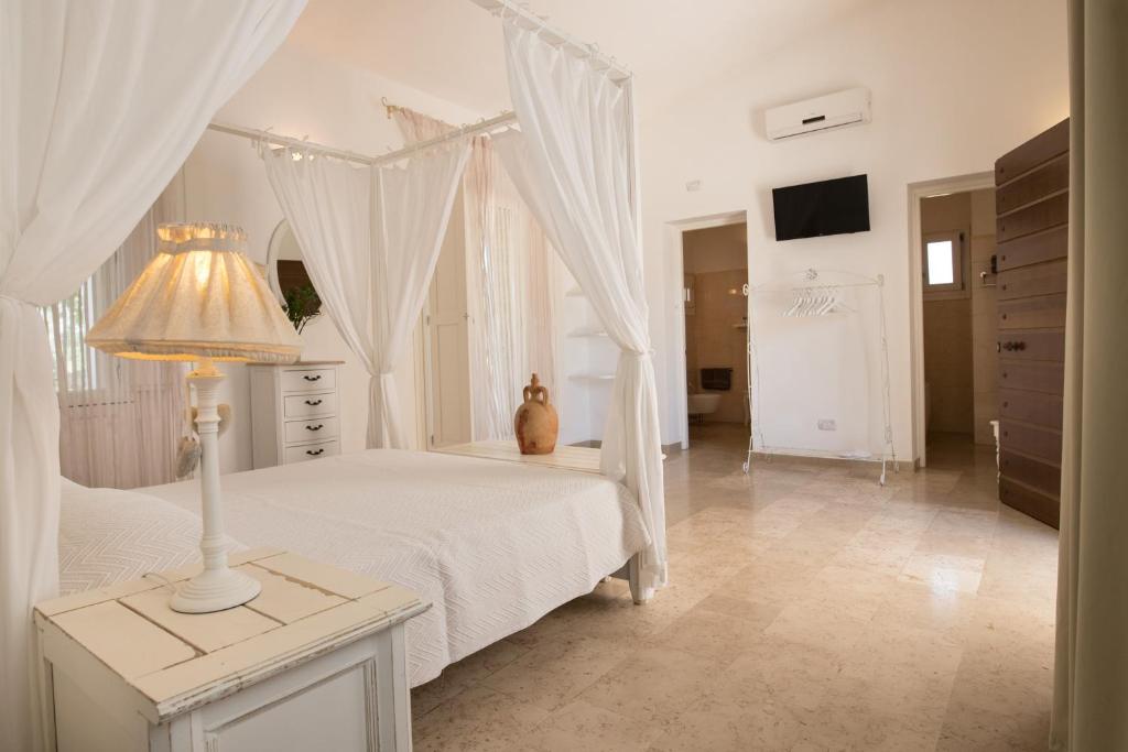 a white bedroom with a white canopy bed and a lamp at Antica Masseria Ficazzana - Tenuta in Marina di Pescoluse