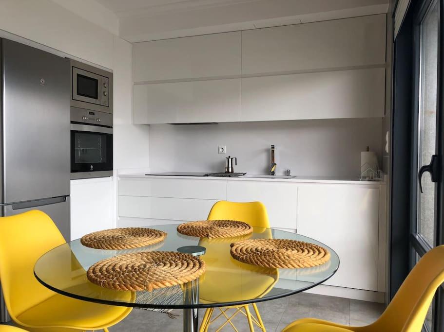 a kitchen with a glass table and yellow chairs at Piso en la Playa in Ribeira