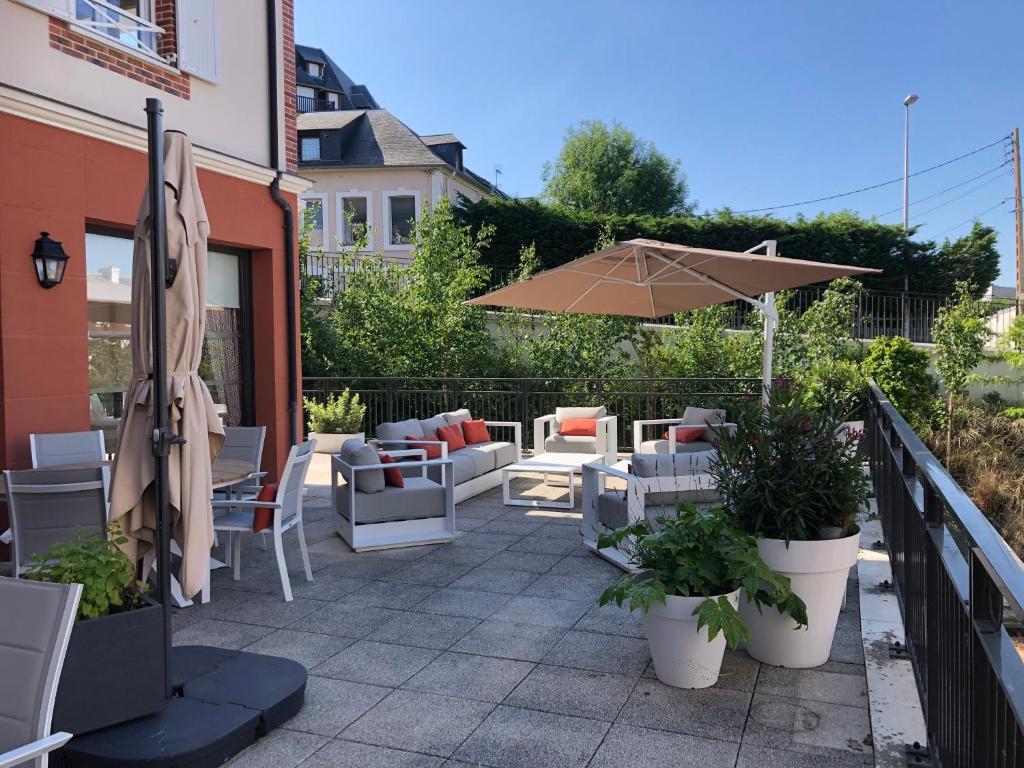 a patio with chairs and an umbrella anditures at Villa Médicis Trouville-sur-mer in Trouville-sur-Mer