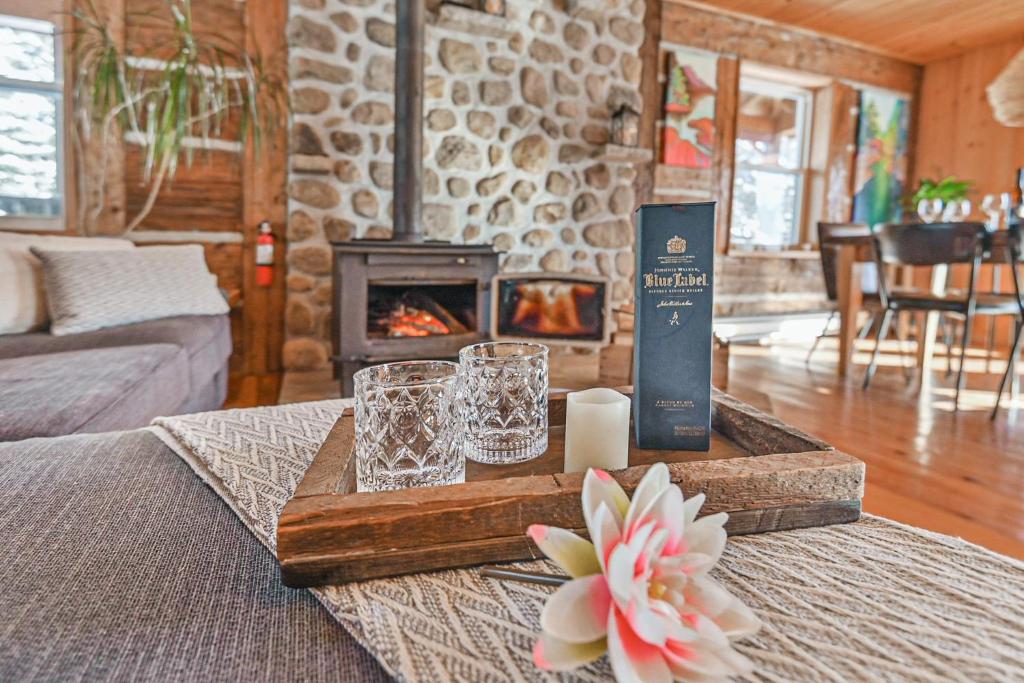 a living room with a table with glasses and a fireplace at River Rock Retreat in Notre-Dame-de-la-Merci