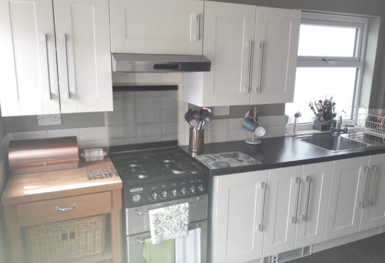 a kitchen with white cabinets and a stove top oven at Porthcawl cottage in Newton