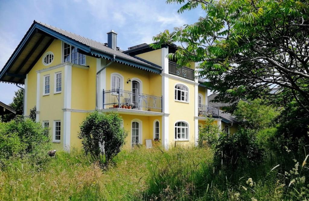 ein gelbes Haus mit einem Balkon an der Seite in der Unterkunft Ferienwohnung in seenaher Künstlervilla in Gstadt in Gstadt am Chiemsee