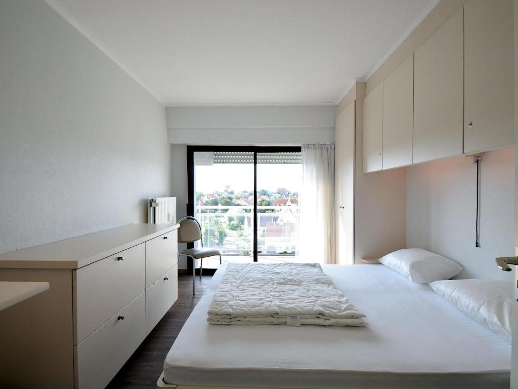 a white bedroom with a large bed and a window at Golf 0401 seafront apartment with balcony in De Haan