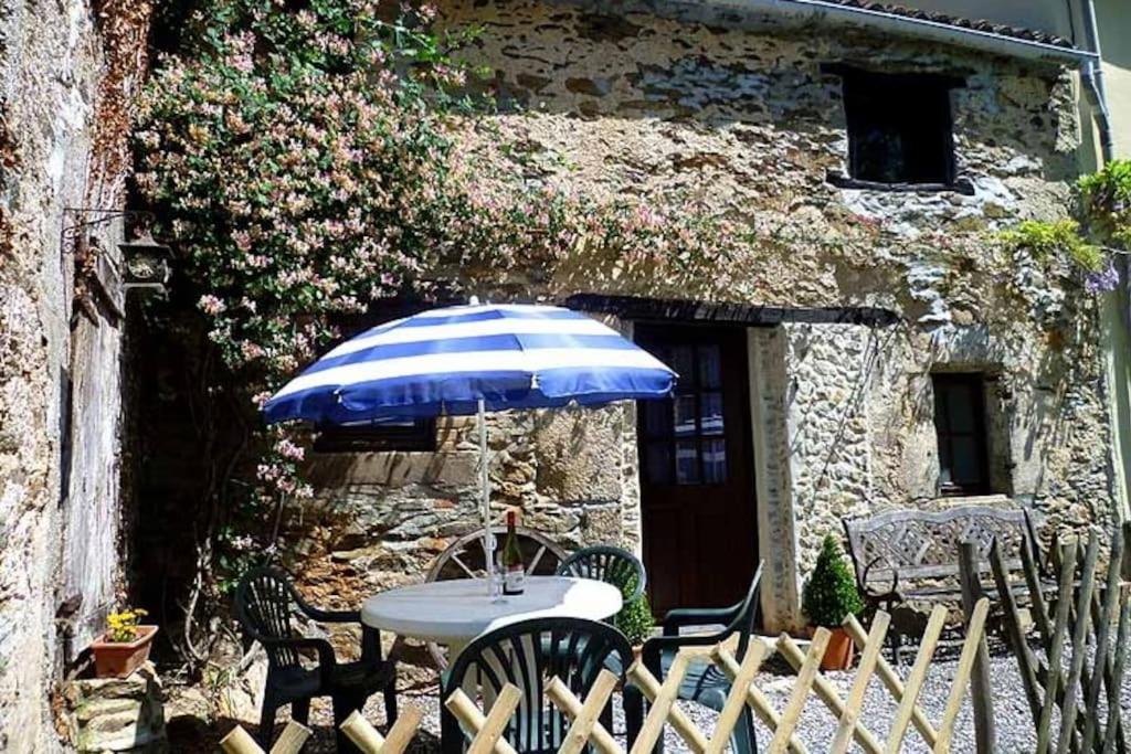 a table and chairs with an umbrella in front of a building at Les Petites Pierres- rural + wifi,pool(shared),games field in Vernoux-en-Gâtine