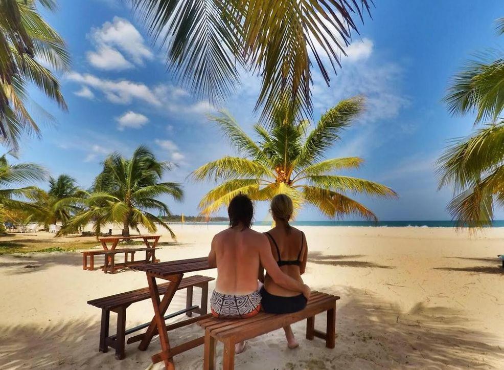 dos personas sentadas en un banco en la playa en Aqua Marine Beach Hotel en Kalkudah