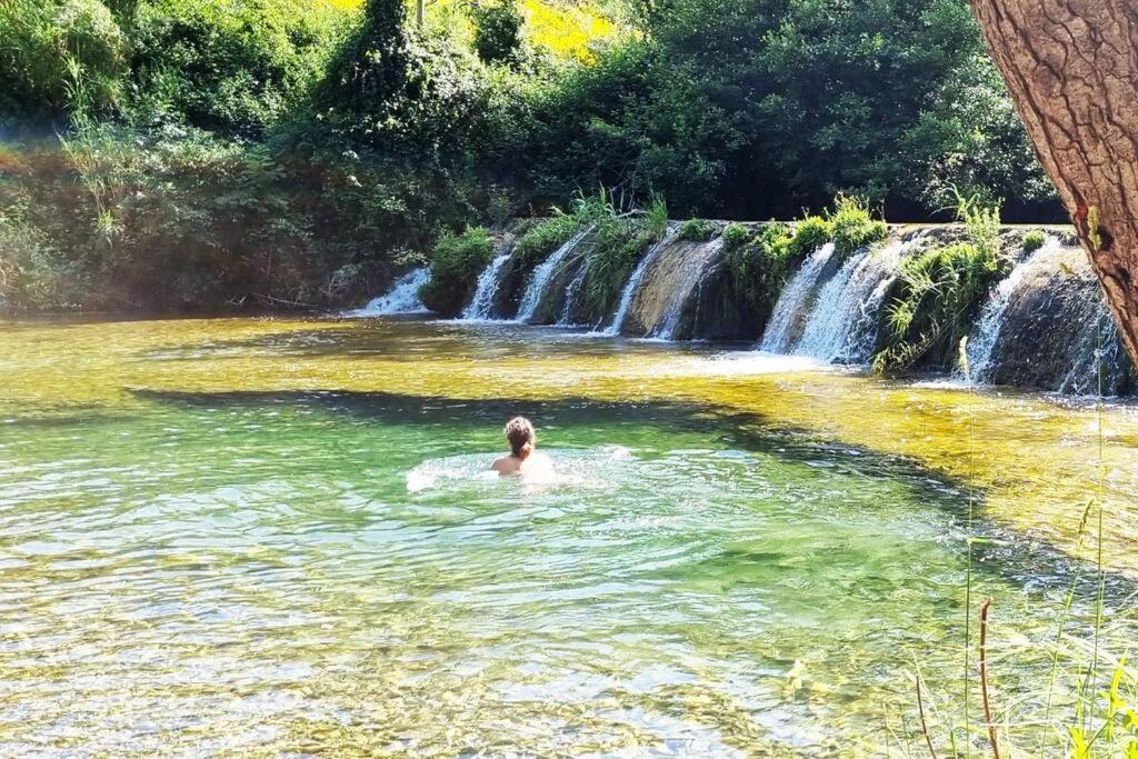 Un uomo che nuota in una piscina di fronte a una cascata di Gîte de la confluence a Padern