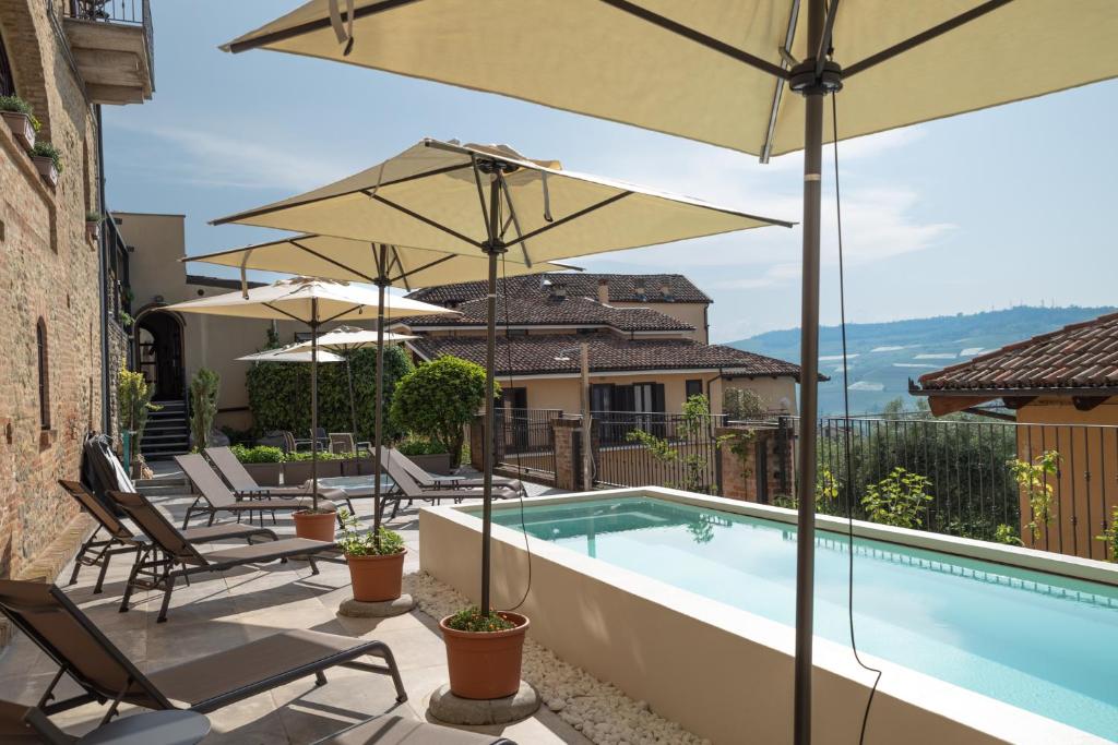 a swimming pool with umbrellas and chairs next to a house at Le Torri - Castiglione Falletto in Castiglione Falletto