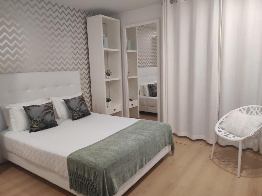 ein weißes Schlafzimmer mit einem Bett und einem Stuhl in der Unterkunft By the Sea in Nazaré