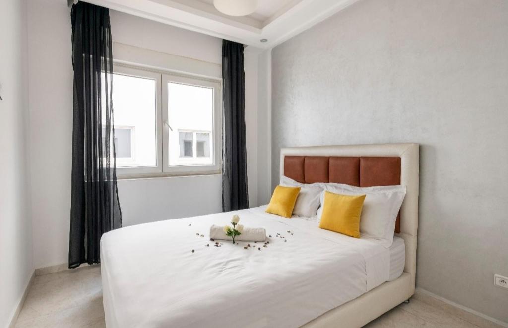 1 dormitorio con 1 cama blanca grande con almohadas amarillas en Appartement 3 CHAMBRES ensoleillé à 5 min de la plage El Jadida en El Jadida
