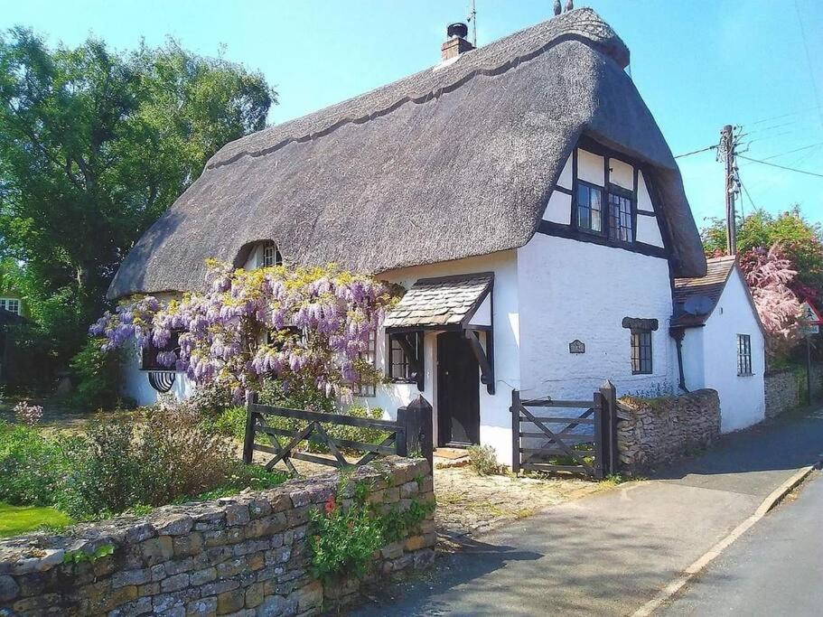 a thatched cottage with a wreath of purple flowers at Cider Mill Cottage in Alderton