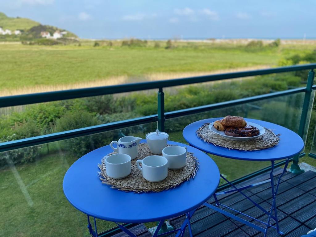 2 mesas azules con tazas y comida en el balcón en Les cygnes de Criel-sur-Mer, en Criel-sur-Mer