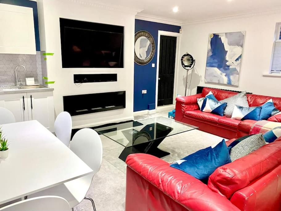 a living room with red leather couches and a tv at The Lodge Annex - immaculate coastal property in Oystermouth