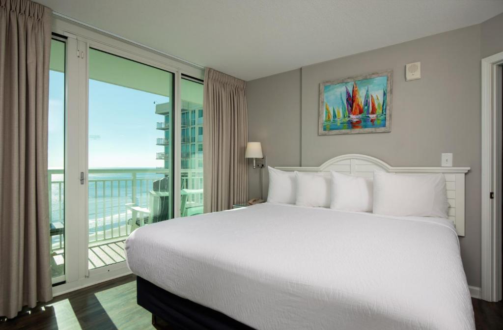 a bedroom with a large white bed and a balcony at Avista Resort in Myrtle Beach