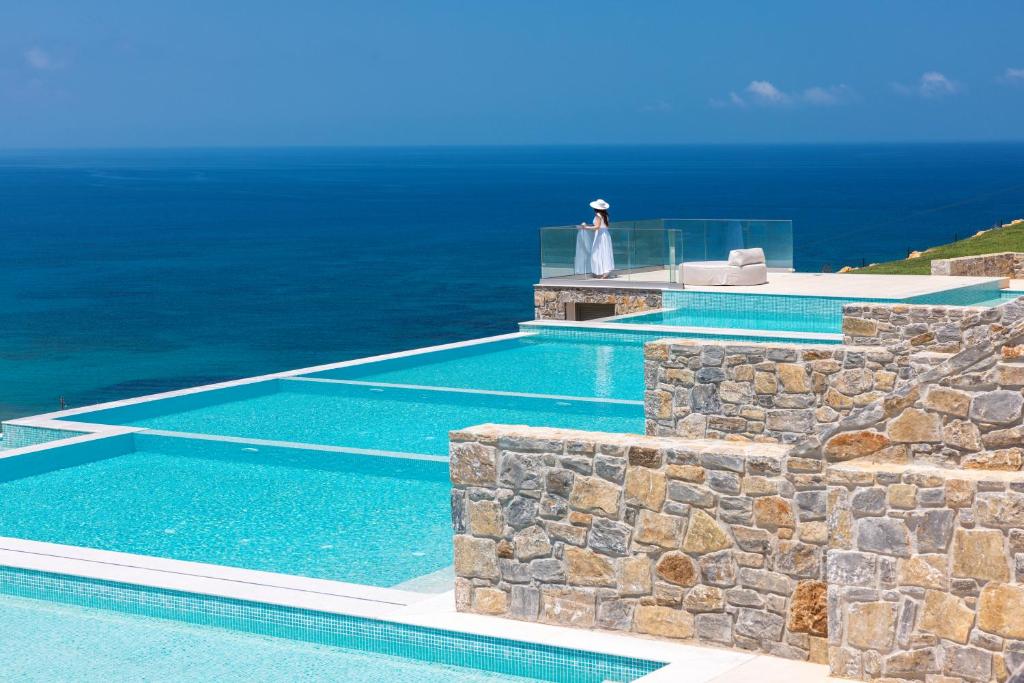 une femme debout à côté d'une piscine avec l'océan dans l'établissement DEDALOS TOUCH BOUTIQUE HOTEL, à Skaleta