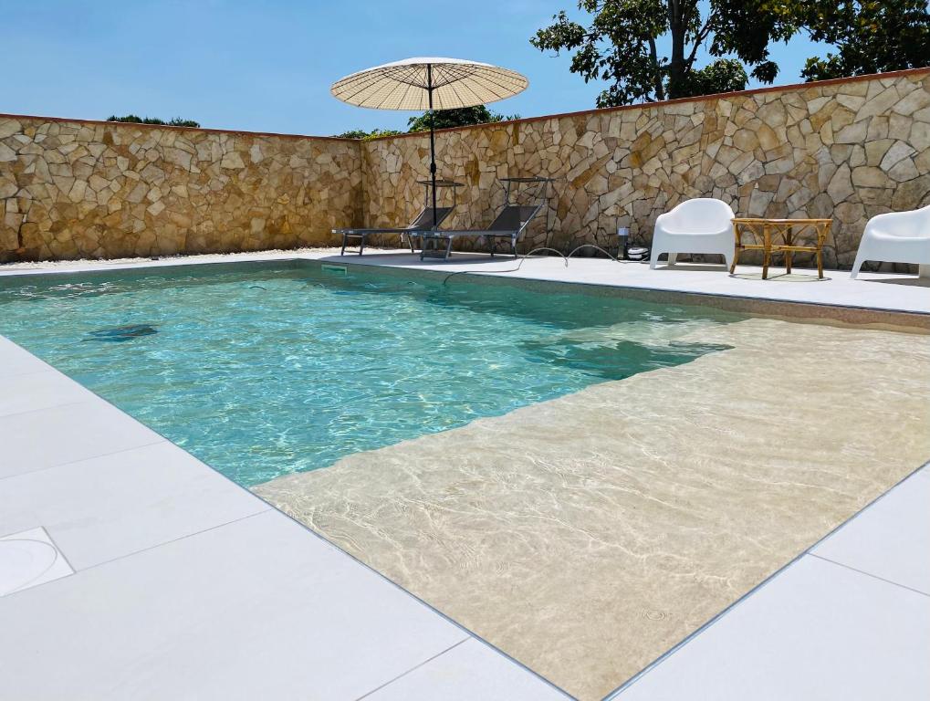 a swimming pool with chairs and an umbrella at Villa Carmen con piscina in Siracusa