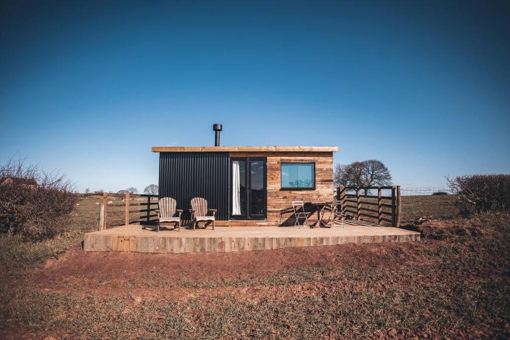 a small cabin in a field with two chairs at 'Cinnabar Nest' Remote Off-Grid Eco Cabin in Sedgefield