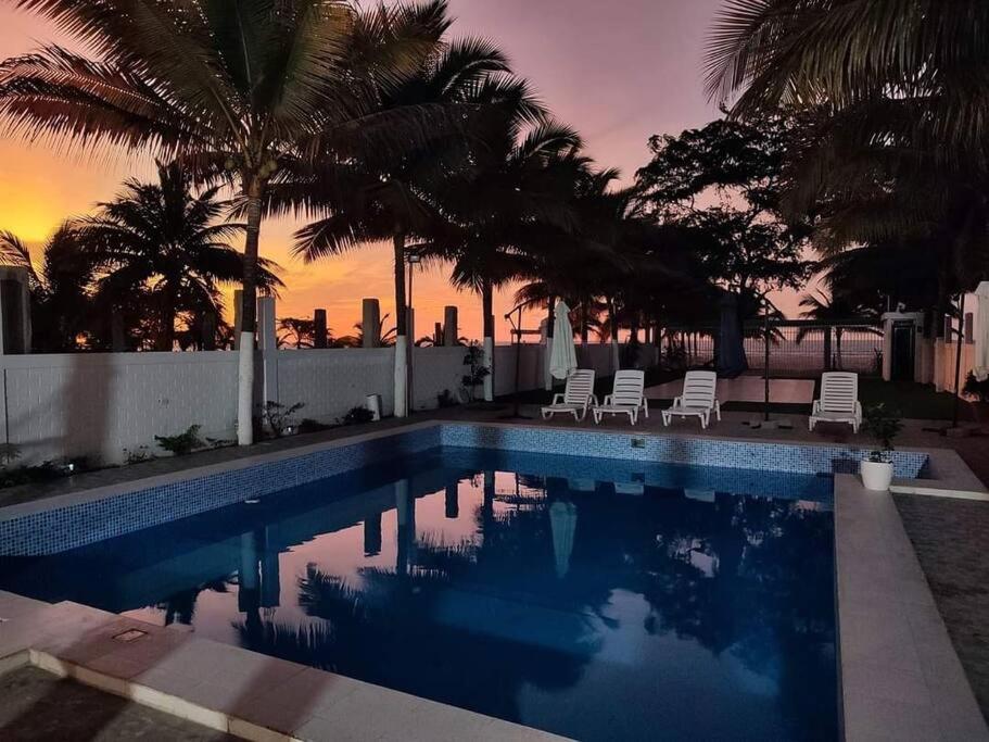 a swimming pool with chairs and palm trees at sunset at Casa de playa Palmeras in Tumbes