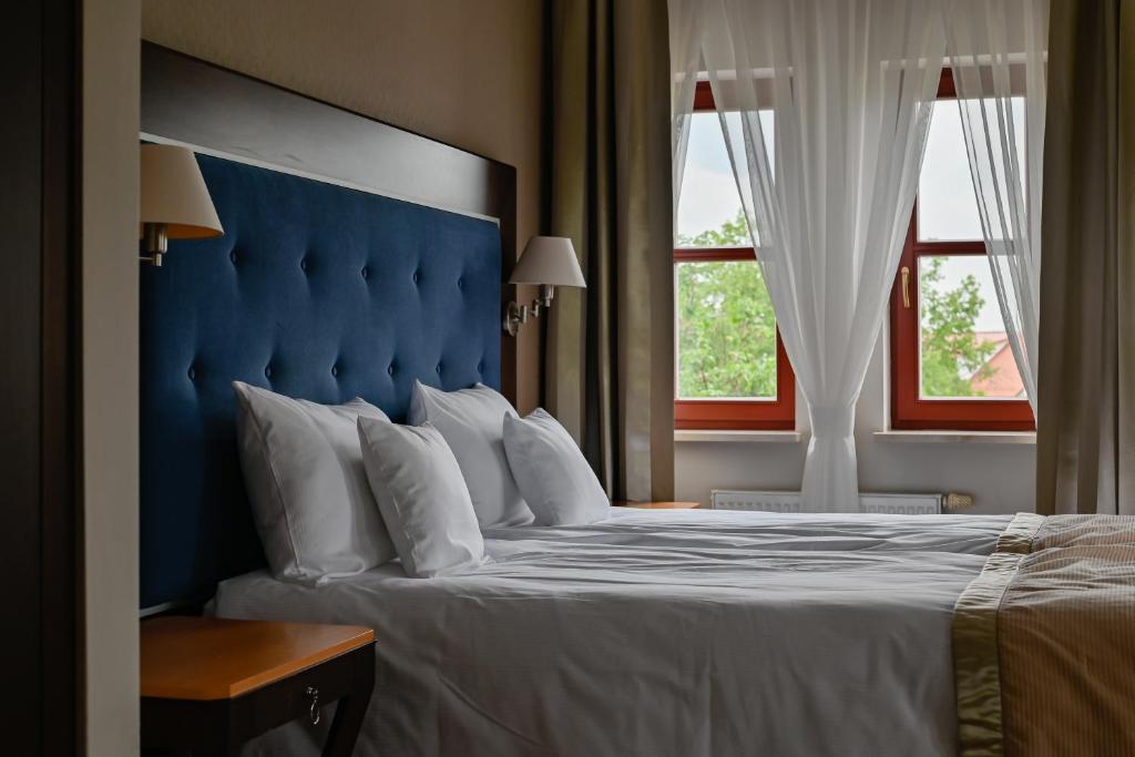 a bed with a blue headboard and two windows at Villa Garden Dyplomat in Olsztyn