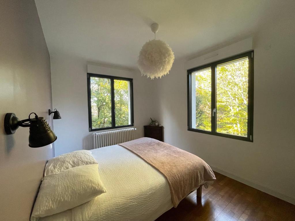 a bedroom with a bed and two windows at Les jardins de l'Hermitage in Cellettes