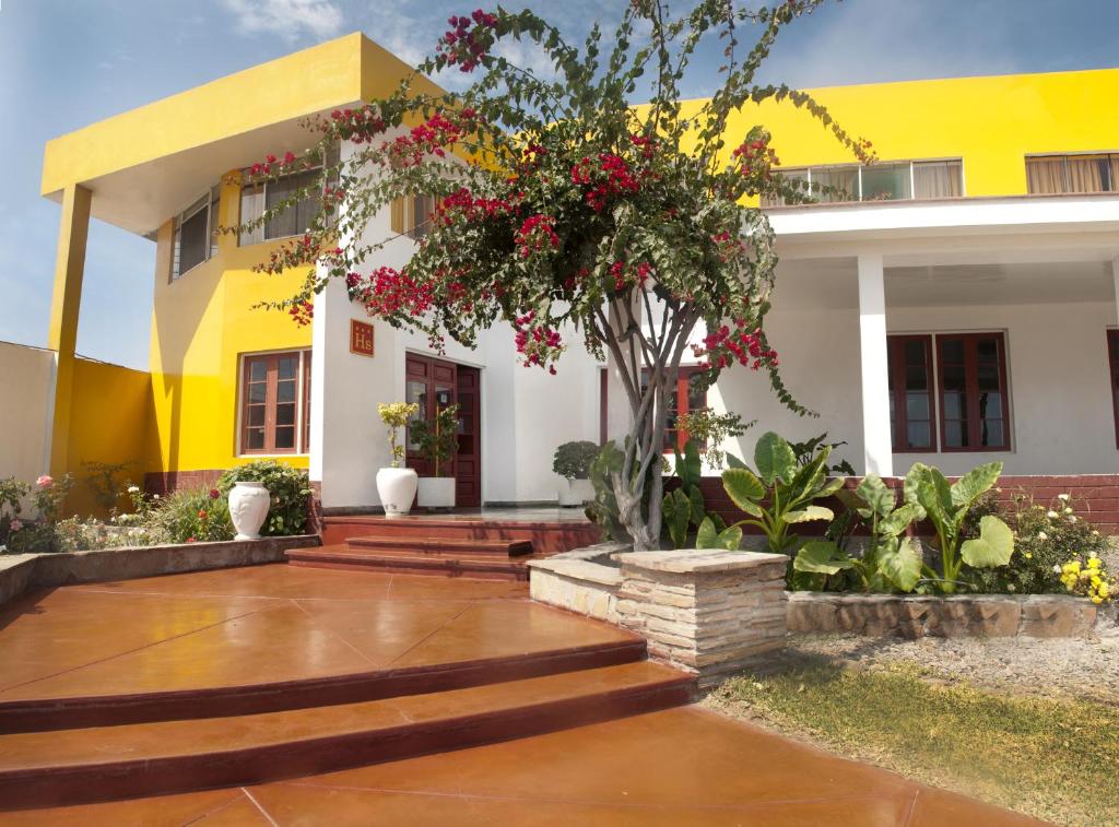 ein gelbes und weißes Haus mit einem Baum und Blumen in der Unterkunft Hostal Miramar in Pisco
